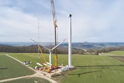 Drone shot of the erection of a wind turbine. A crane lifts the rotor star.